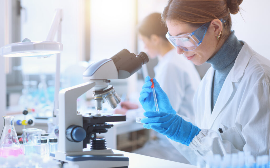 Young female student in the research lab, she is examining a sample in a petri dish and using the microscope