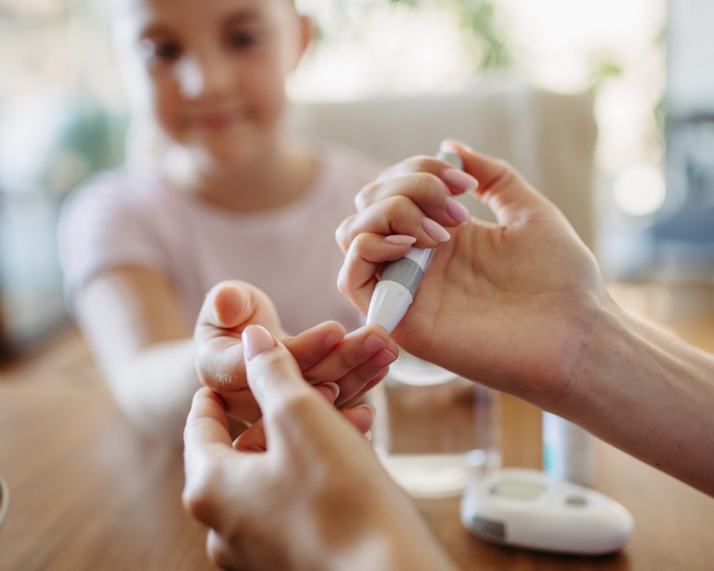 Close up of mother checking girl's blood glucose level using a fingerstick glucose meter. Endocrinologist waiting for results from blood test.