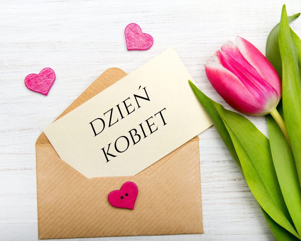 Women's day card with Polish words DZIEŃ KOBIET. Tulip  and envelope on white wooden background